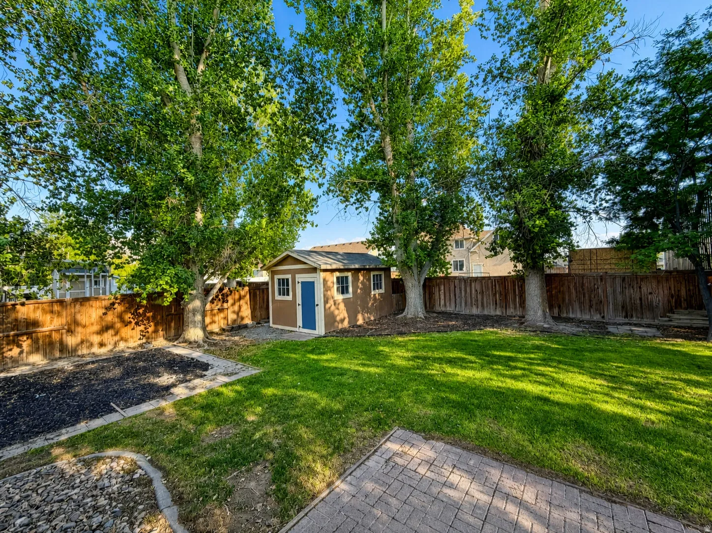 Expansive backyard featuring a manicured lawn, established trees, privacy fencing, and a storage shed with a blue door
