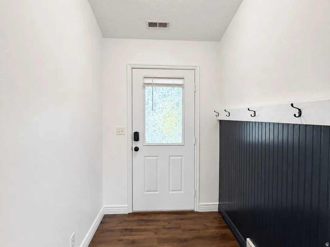 Wood-finish flooring, white paneled door with frosted glass, built-in coat hooks, and beadboard wall accent