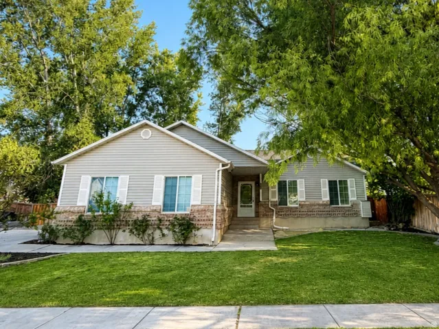 Light gray siding exterior with stone veneer accents, white window shutters, a large mature tree, and a manicured lawn