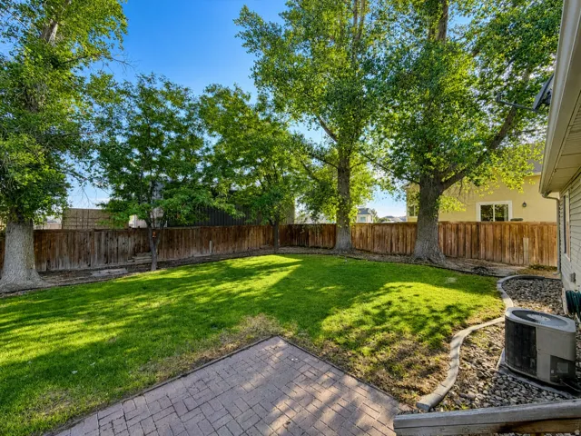 Expansive backyard featuring a manicured lawn, established shade trees, wood privacy fencing, and a paver patio