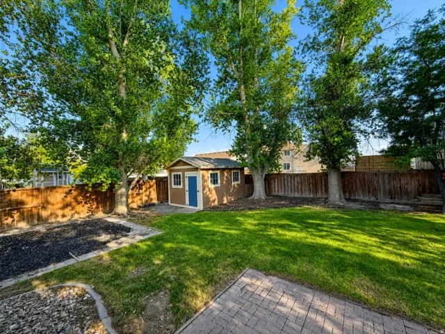 Expansive backyard featuring a manicured lawn, established trees, privacy fencing, and a storage shed with a blue door