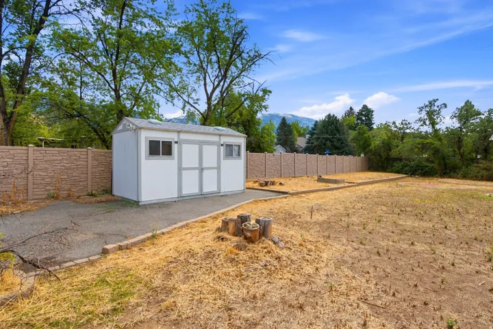 Expansive outdoor space featuring a detached storage shed with dual doors and windows, a paved pathway, and a perimeter fence
