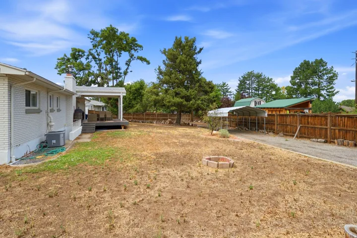 Covered patio, brick exterior, gravel driveway, wood fencing, and an uncovered fire pit