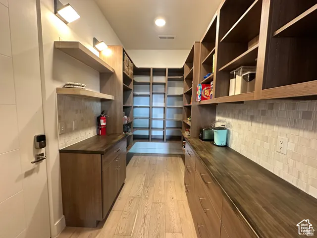 Expansive pantry featuring extensive built-in shelving, wood-finish flooring, wood-finish cabinetry, and solid surface countertops
