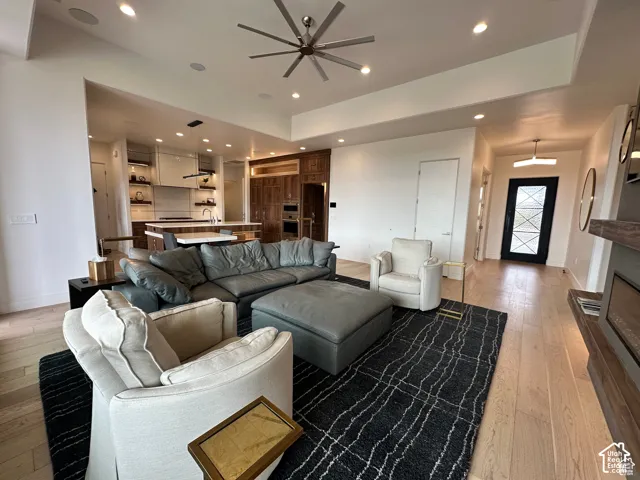 Recessed ceiling lighting, ceiling fan, wood-finish flooring, built-in fireplace, and a black entry door with decorative glass panels