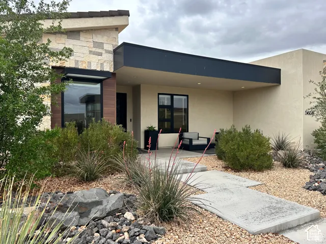 Exterior featuring stacked stone accents, wood-finish siding, a covered entry, and a contemporary landscape design with decorative rock and plantings
