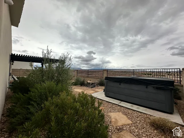 Patio area featuring a covered hot tub, stone stepping pads, low-maintenance landscaping, and a pergola