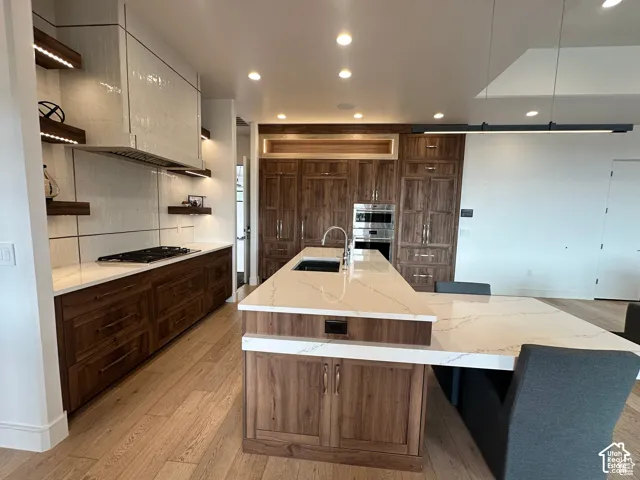 Modern kitchen featuring custom wood-finish cabinetry, white quartz countertops, a dual-island layout with waterfall edge detail, stainless steel built-in appliances, recessed and pendant lighting, and wide-plank wood-finish flooring throughout