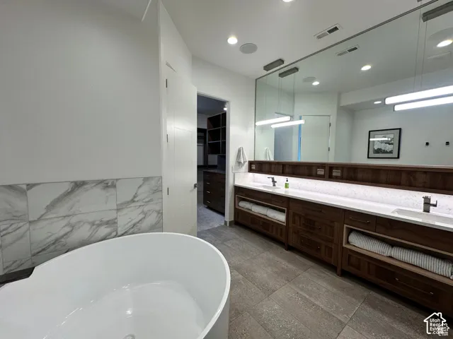 Freestanding soaking tub, large format floor tiling, dual vanity with undermount sinks, and wall-mounted faucets