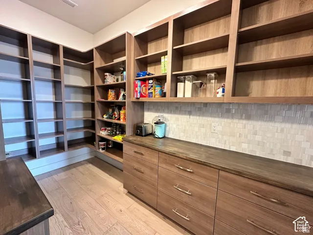 Custom built-in shelving, wood-finish flooring, ample counter space, integrated drawers, and a mosaic tile backsplash