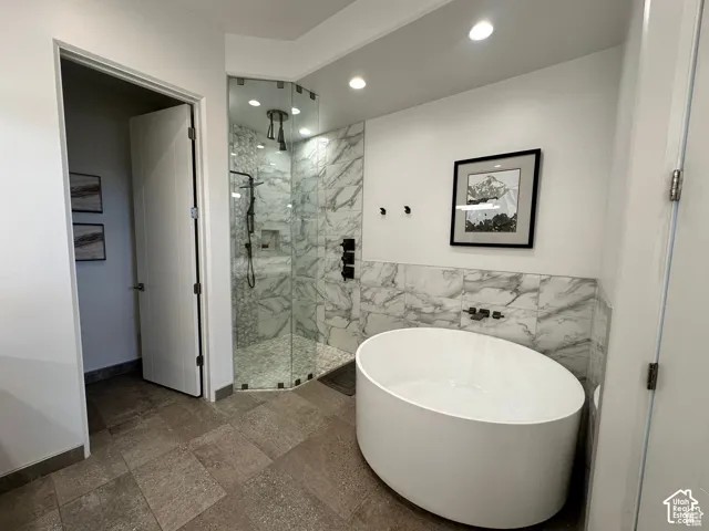 Freestanding oval soaking tub, expansive glass-enclosed shower, marble-finish tile walls, large format floor tiles, and recessed lighting