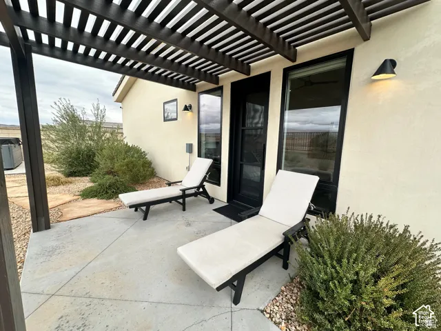 Exterior patio featuring a slatted pergola, concrete flooring, exterior wall sconces, and a stucco finish