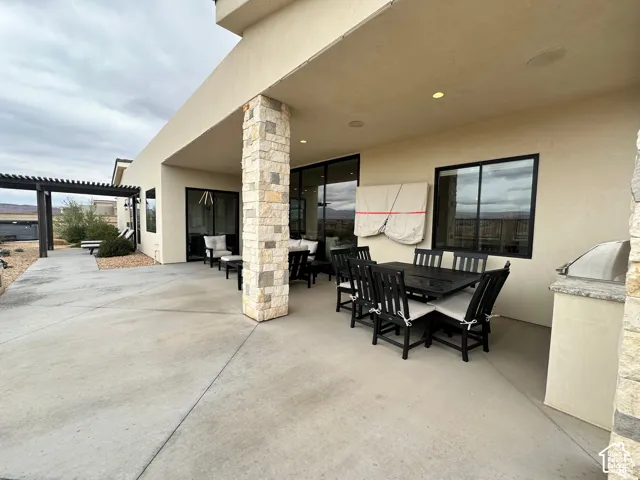 Spacious covered patio with stone pillar accents, integrated recessed lighting, an outdoor built-in grill, and an additional uncovered patio area with a pergola