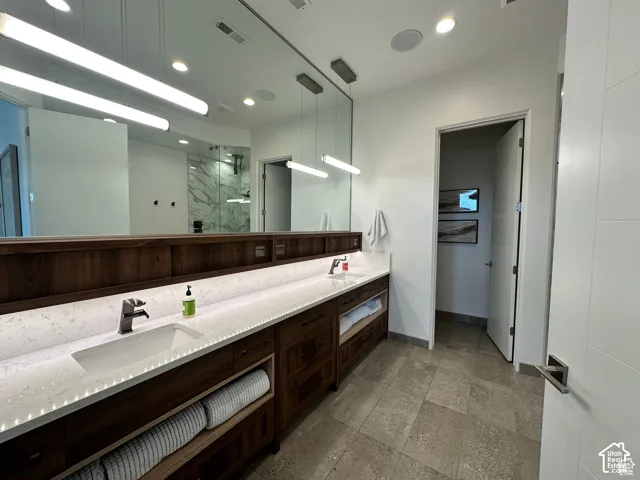 Dual vanity with integrated sinks, wood-finish cabinetry, quartz countertops, and a full-width wall mirror