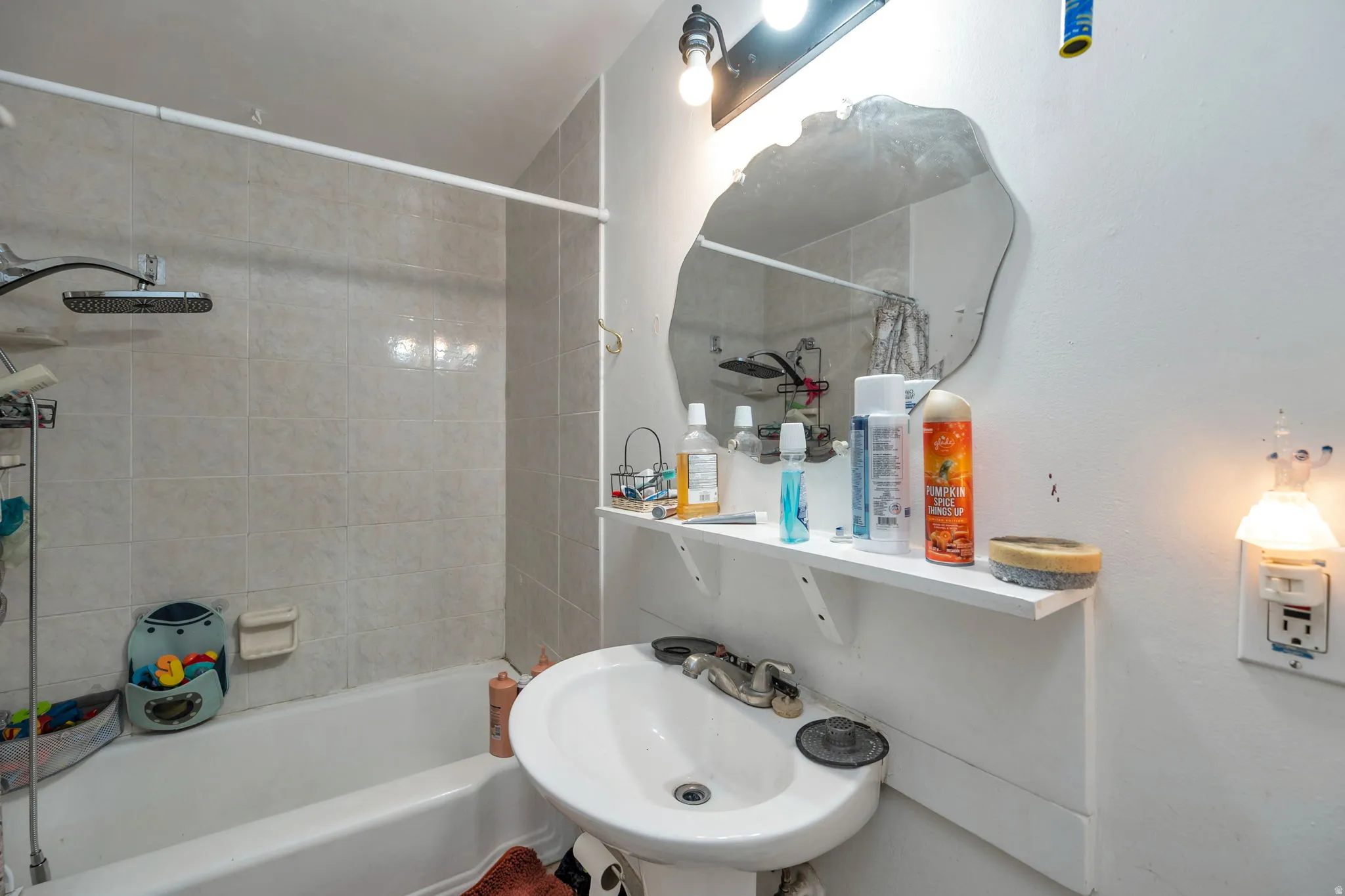 Bathroom featuring a pedestal sink with chrome fixtures, framed mirror, tile shower surround with glass enclosure, and floating shelving with ample storage for toiletries and essentials