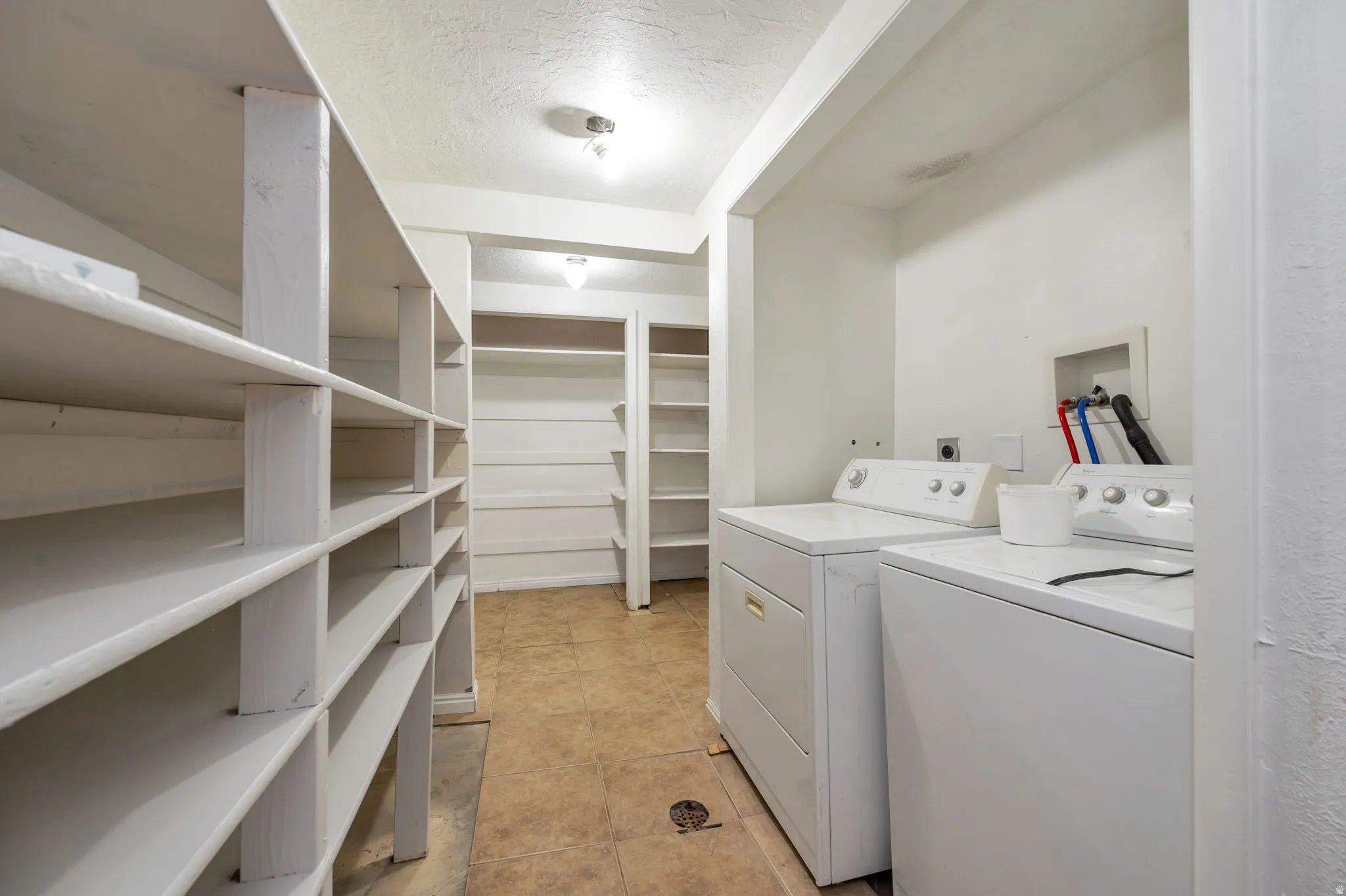 Spacious laundry room featuring white cabinetry with generous shelving throughout, stacked washer and dryer units, wood-finish flooring, and recessed ceiling lighting