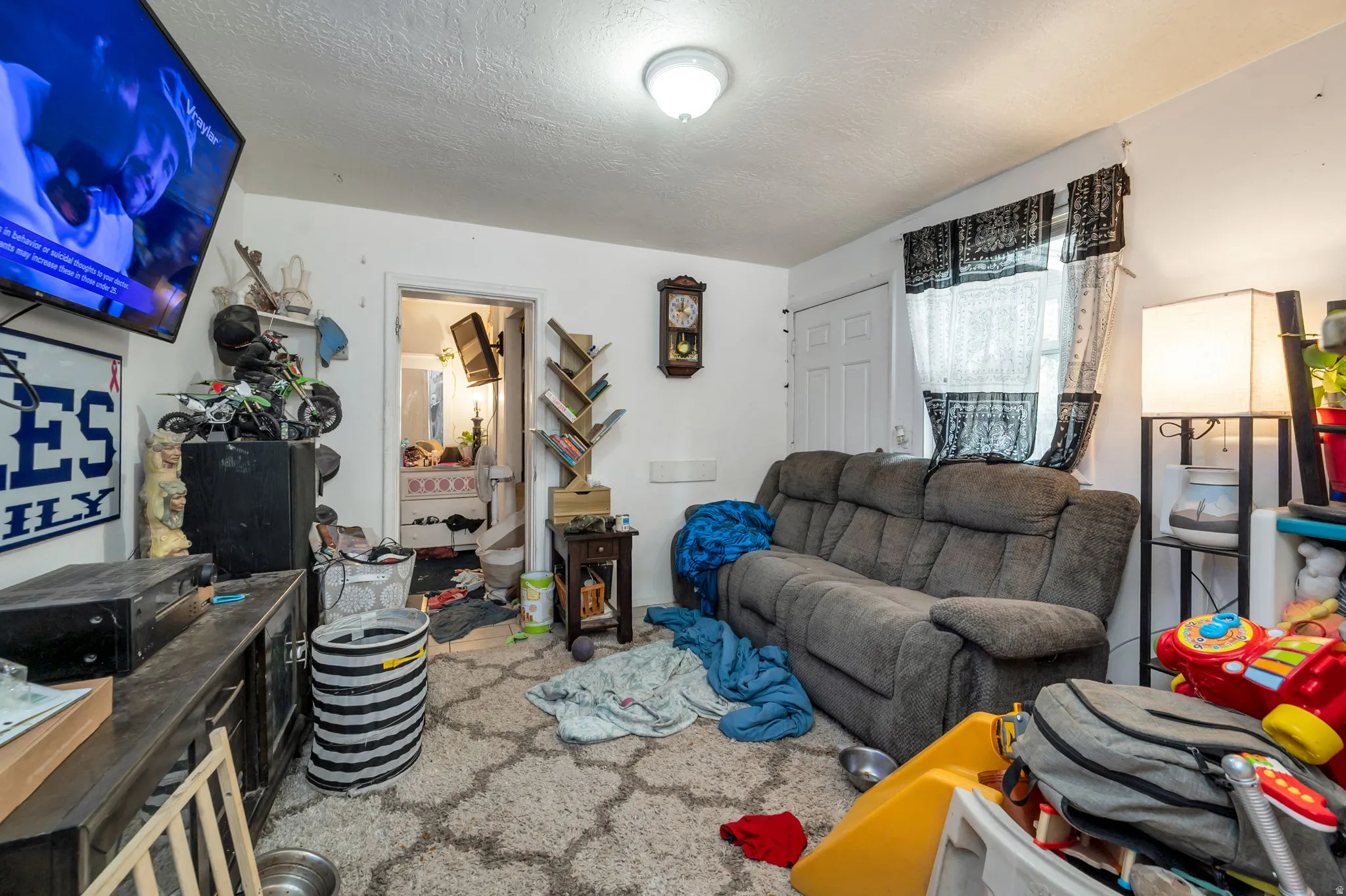Additional contentThe image shows a residential living room with significant clutter, scattered items, and personal belongings throughout the space