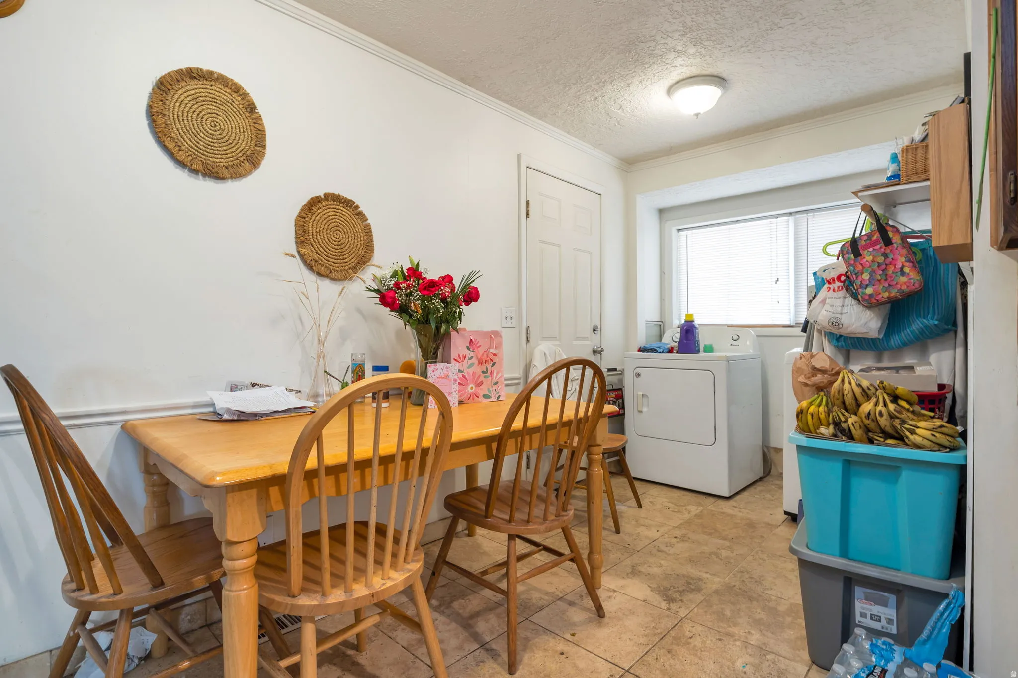 Spacious dining area featuring a wood-finish table with Windsor-style seating, ceramic tile flooring, and abundant natural light from multiple windows