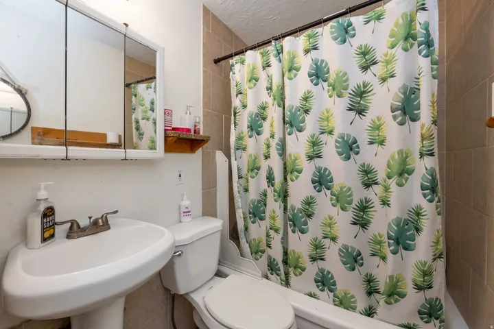 Full bathroom featuring a curved pedestal sink with widespread faucet, toilet, and tile surround