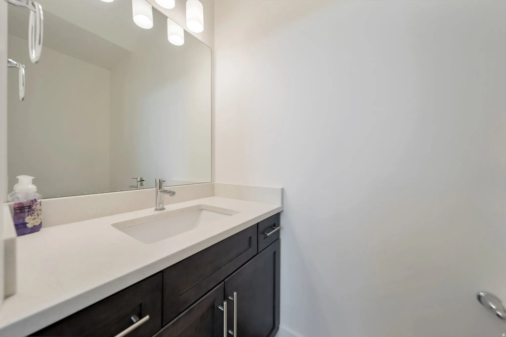 Dark wood-finish vanity with chrome hardware, an integrated rectangular sink, a light-toned countertop, and a wall-mounted mirror with overhead lighting