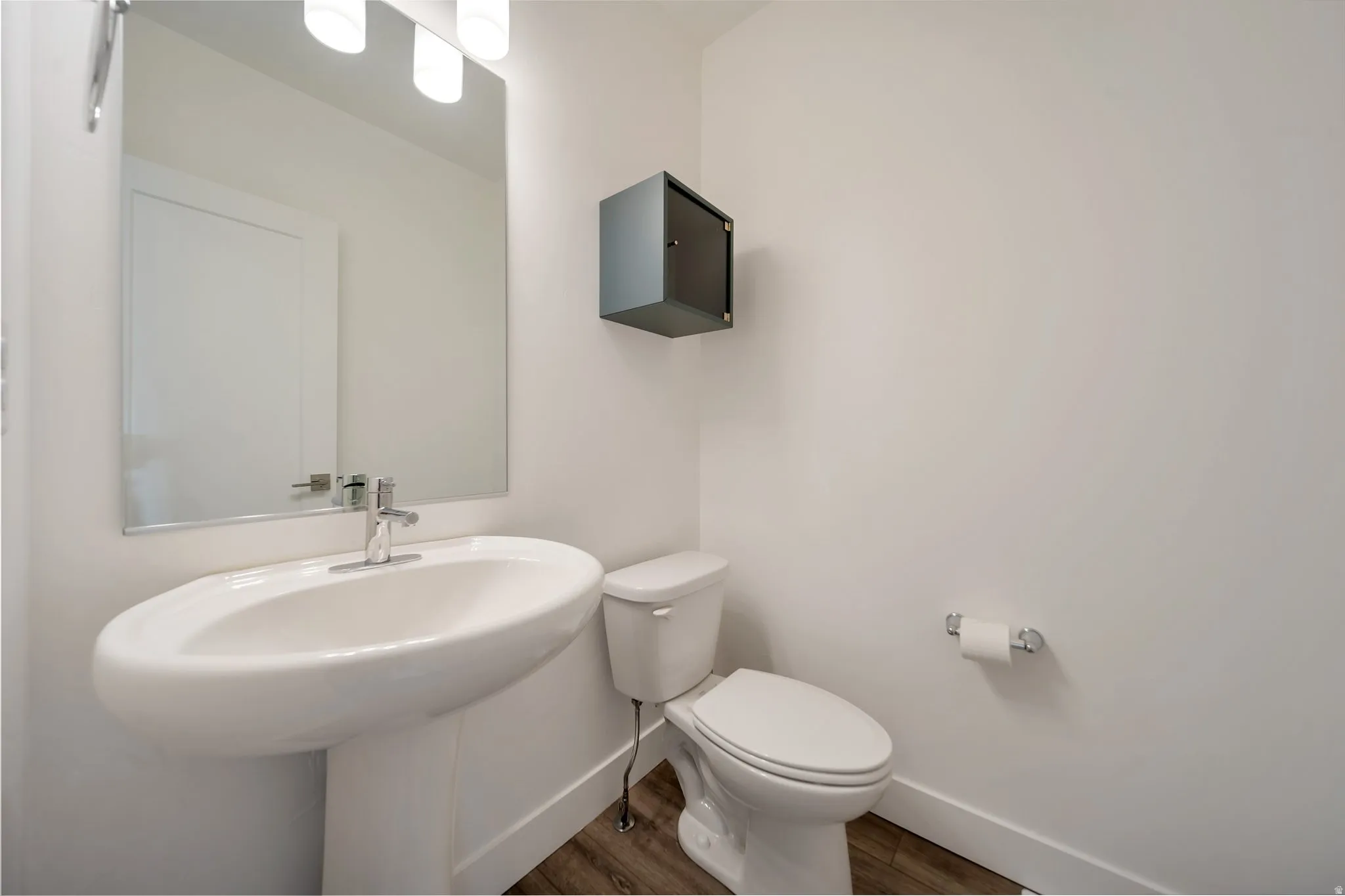 Pedestal sink with chrome faucet, large rectangular mirror, and wood-finish flooring