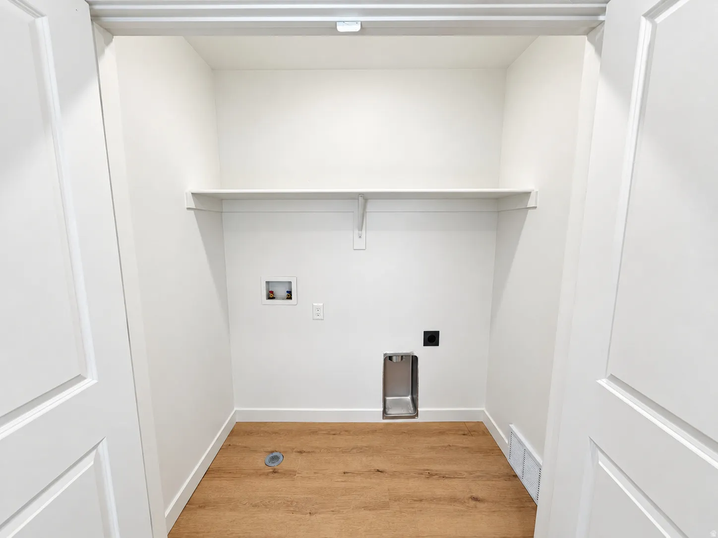 Laundry closet with wood-finish flooring, built-in shelving, and white paneled doors