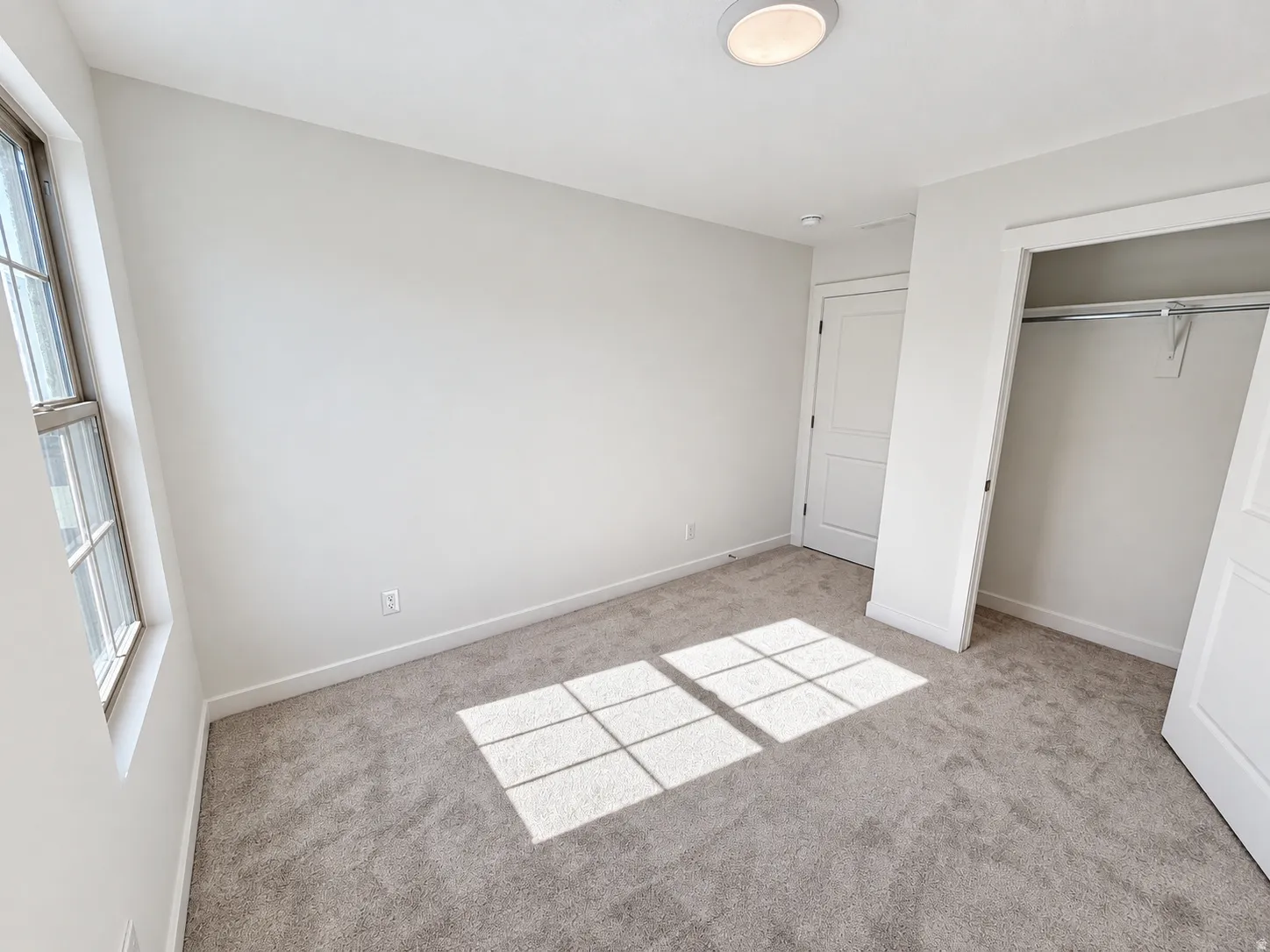 Wall-to-wall carpeting, white walls, double-hung window, flush mount ceiling light, and a built-in closet with shelving