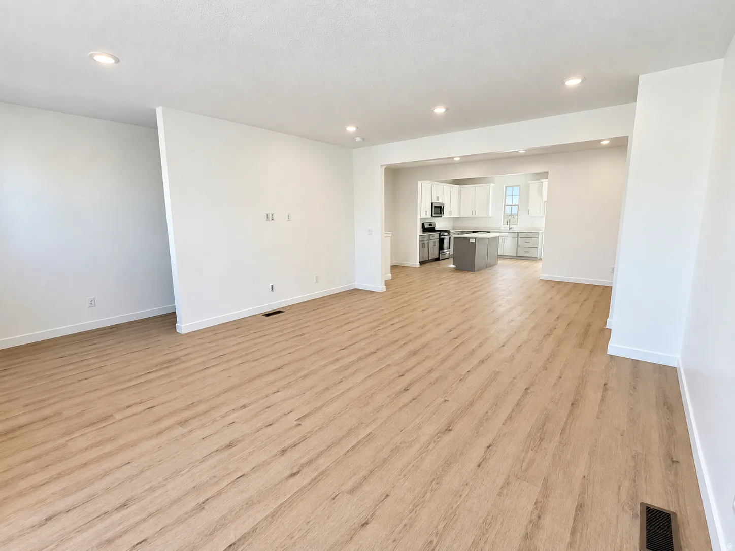 Open-concept living space featuring light wood-finish flooring, recessed lighting, and a kitchen with light-toned cabinetry, a central island, and stainless steel appliances