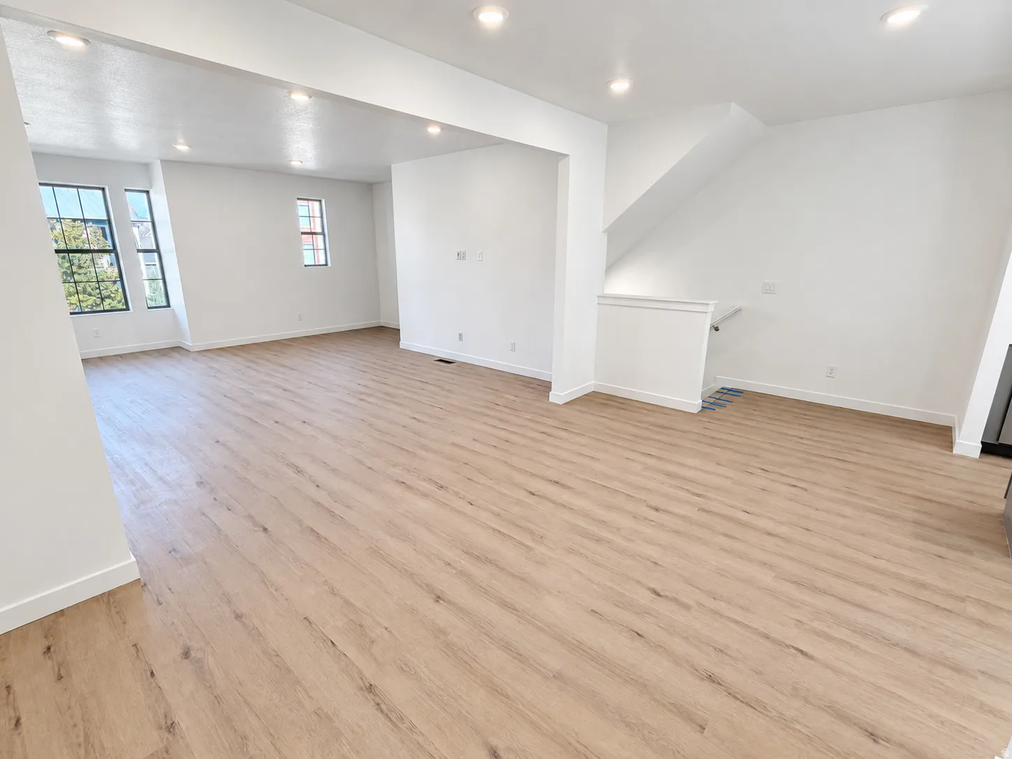 Spacious open-concept room featuring wood-finish flooring, recessed lighting, white walls, and multiple windows