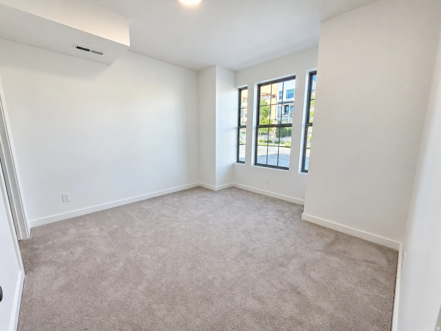 Recessed ceiling light fixture, neutral carpeting, white walls, and multiple windows with black frames