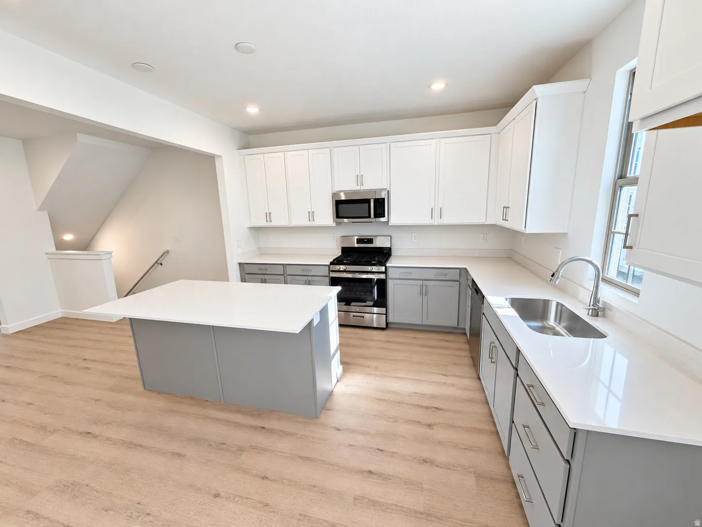 Kitchen featuring a central island with countertop, two-tone cabinetry, stainless steel appliances, and wood-finish flooring