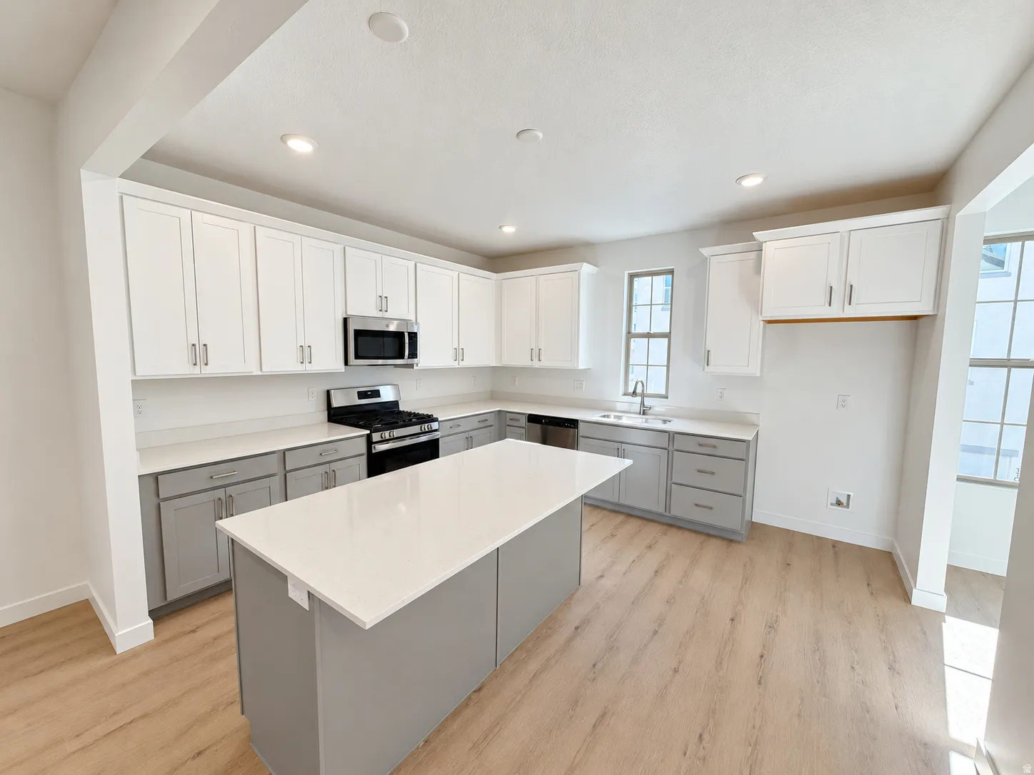 Kitchen featuring an expansive island with a light-toned countertop, two-tone cabinetry, stainless steel appliances, and wood-finish flooring