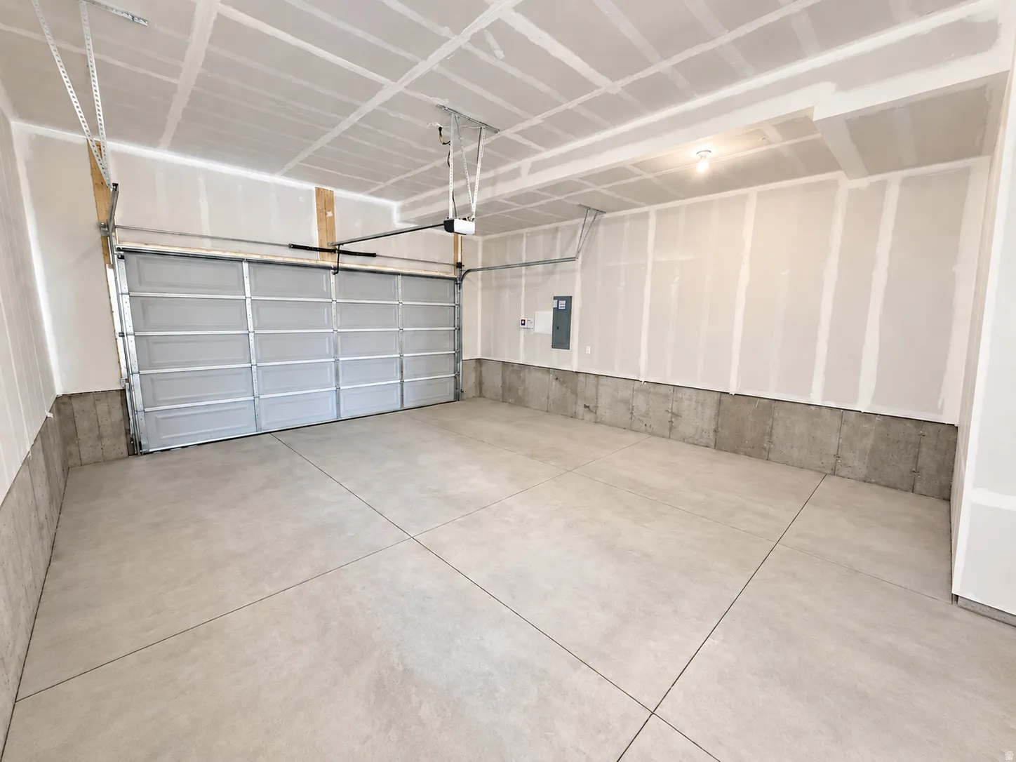 Spacious garage featuring a paneled overhead door, concrete flooring, exposed concrete foundation, and unfinished drywall walls