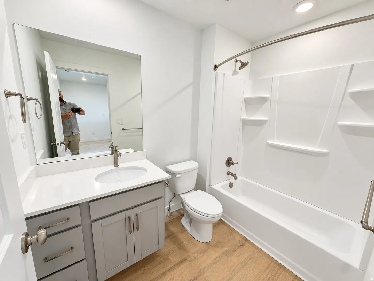 Bathroom featuring a vanity with a white countertop and undermount sink, gray cabinetry, brushed nickel fixtures, and wood-finish flooring