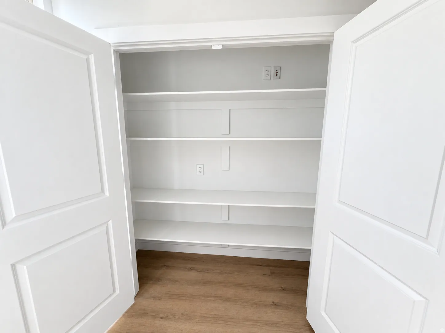 White bi-fold doors open to reveal built-in shelving, wood-finish flooring, and electrical outlets