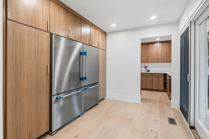 Stainless steel French door refrigerator, full-height wood-finish cabinetry, light wood-finish flooring, recessed ceiling lighting, and sliding glass door