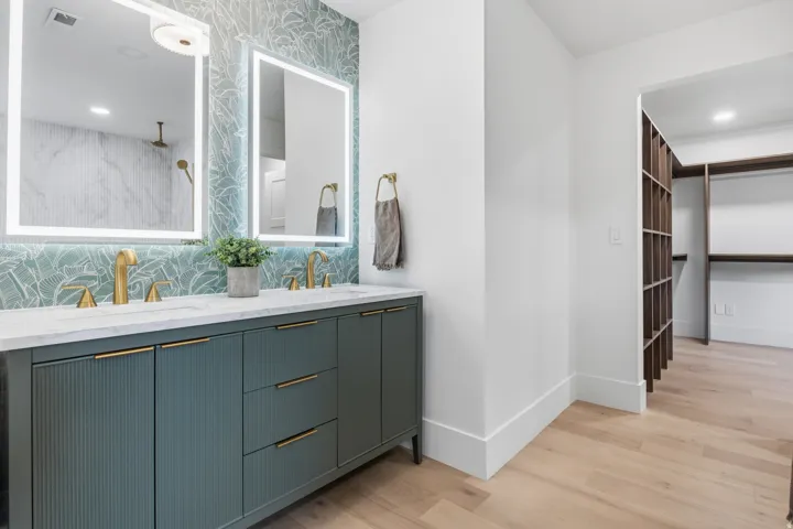 Dual vanity with undermount sinks and brass-finish fixtures, backlit mirrors, and a patterned tile accent wall