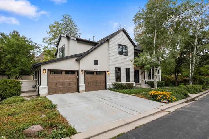 Contemporary architecture featuring a stucco and shingle exterior, dark-framed windows, wood-finish garage doors, and mature landscaping