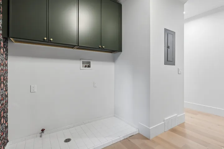 Built-in dark green cabinetry with brass hardware, white tiled floor, light wood-finish flooring, and white baseboards