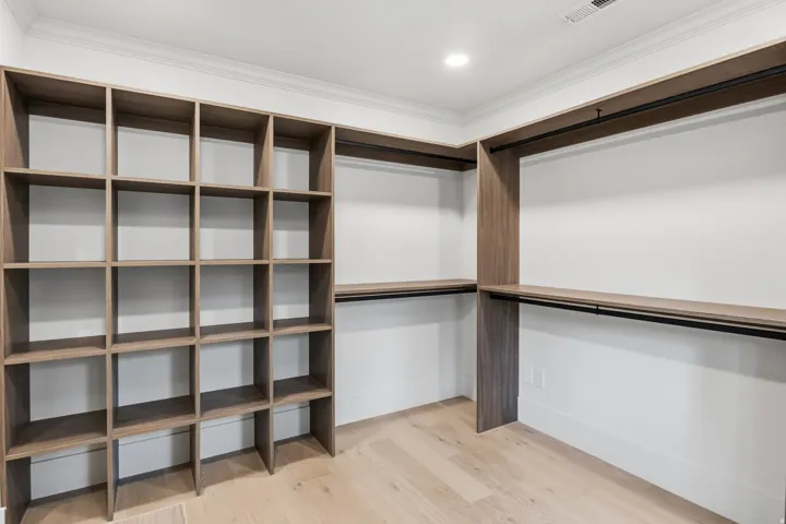 Built-in shelving, wood-finish flooring, recessed lighting, crown molding, and hanging rods