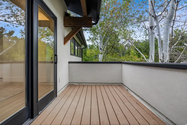 Private balcony with wood-finish decking, stucco exterior, and a sliding glass door