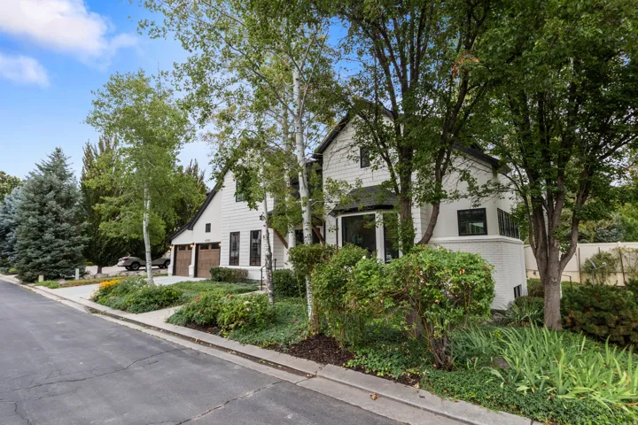 White exterior with dark trim accents, multiple windows, attached garage with wood-finish doors, and established landscaping