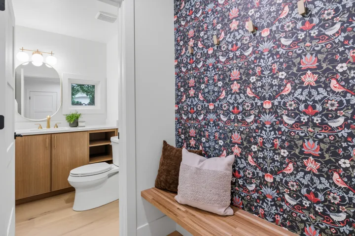 Powder room featuring a wood-finish vanity with countertop, oval mirror, and a three-globe vanity light