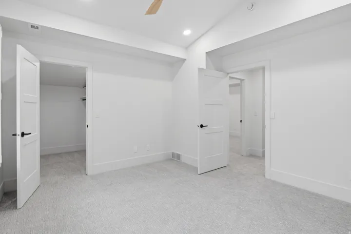 Vaulted ceiling, recessed lighting, light-toned carpet, white interior doors with black hardware, and an integrated ceiling fan