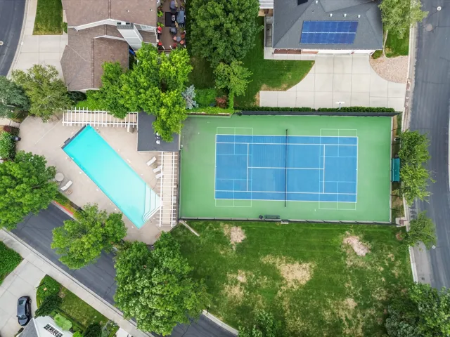 Rectangular swimming pool with surrounding hardscaping, adjacent tennis court, and mature trees