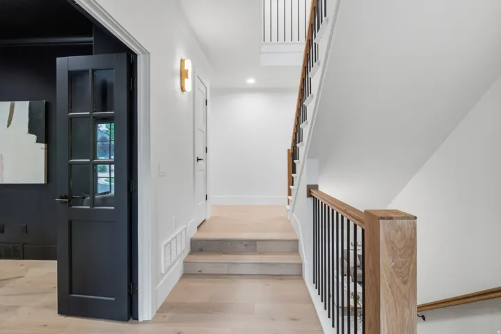 Hardwood flooring, custom staircase with wood handrails and black metal spindles, recessed lighting, and a modern wall sconce