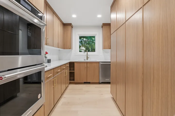 Integrated stainless steel appliances, wood-finish cabinetry, light countertops, wood-finish flooring, and recessed lighting
