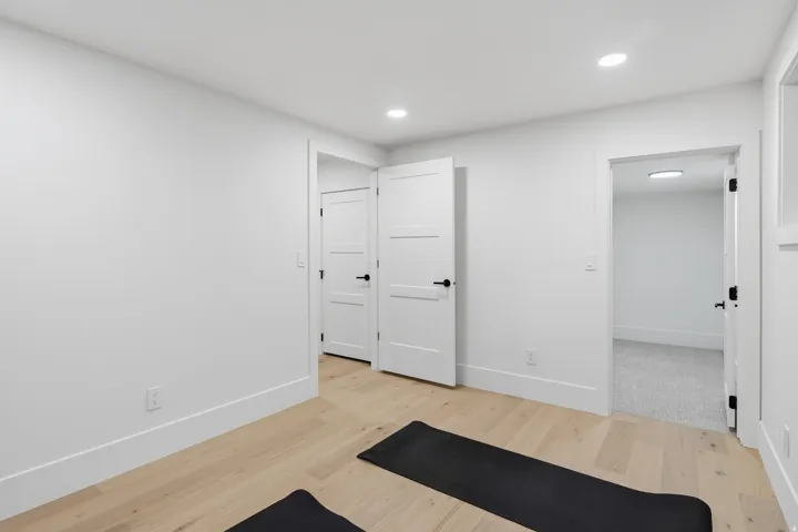 Recessed lighting, wood-finish flooring, white walls, white trim, and a white interior door with black hardware