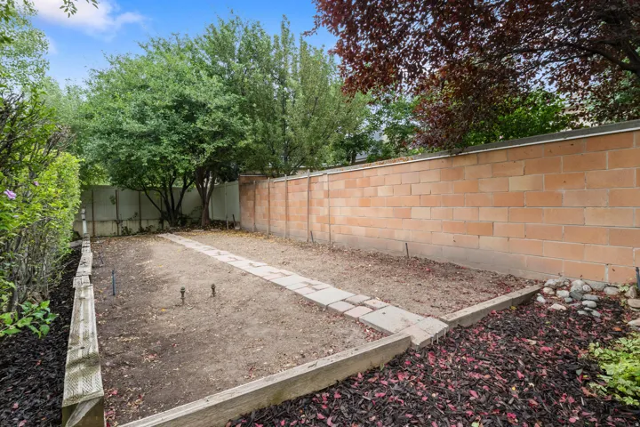 Enclosed yard featuring a block wall, paved pathway, and surrounding garden beds