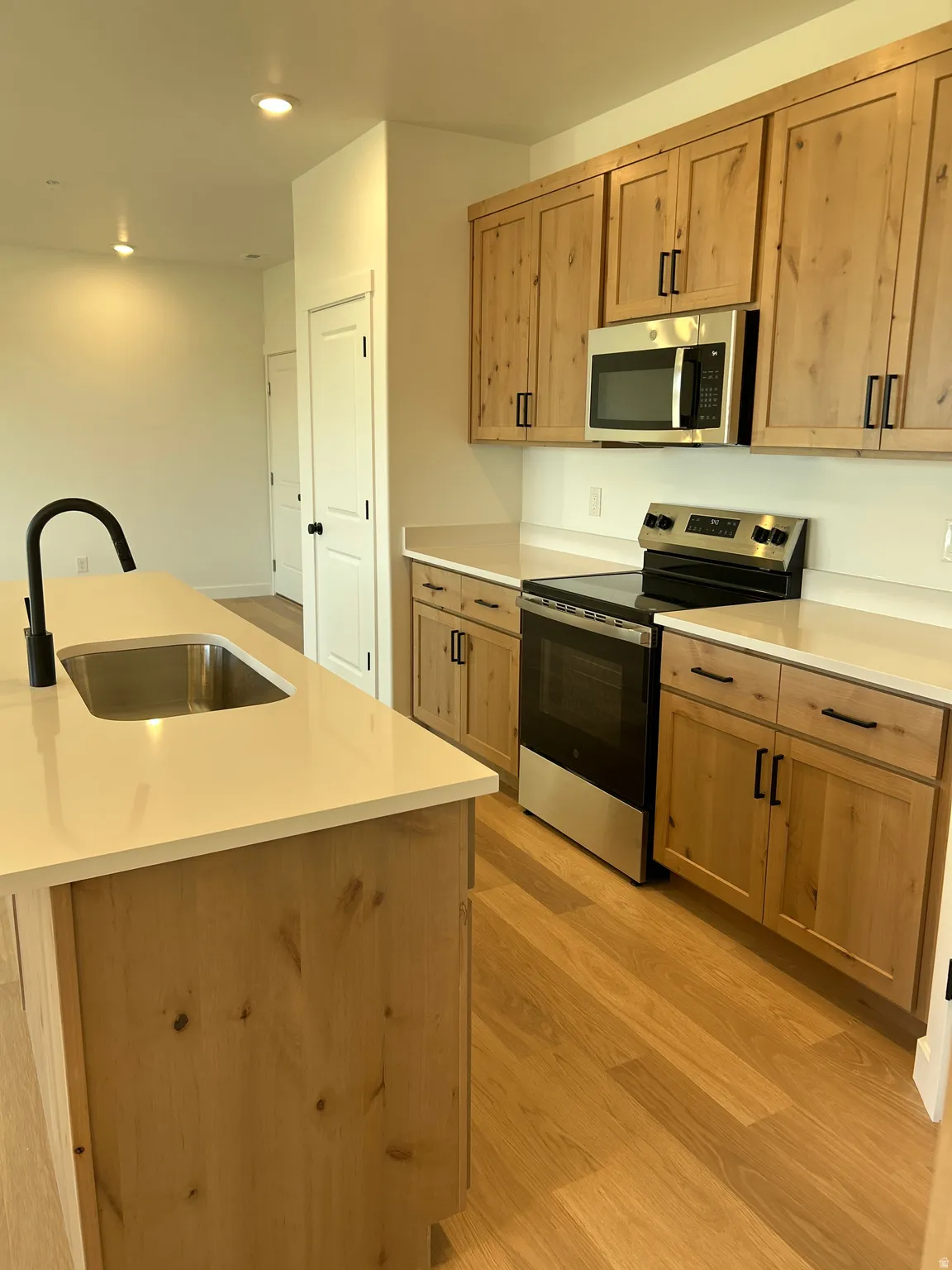 Kitchen featuring wood-finish cabinetry, stainless steel appliances, light-toned countertops, and wood-finish flooring